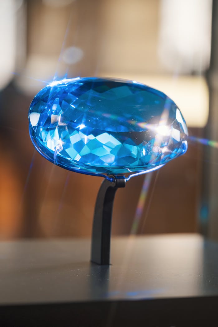 A stunning blue gemstone displayed on a stand, reflecting light beautifully.