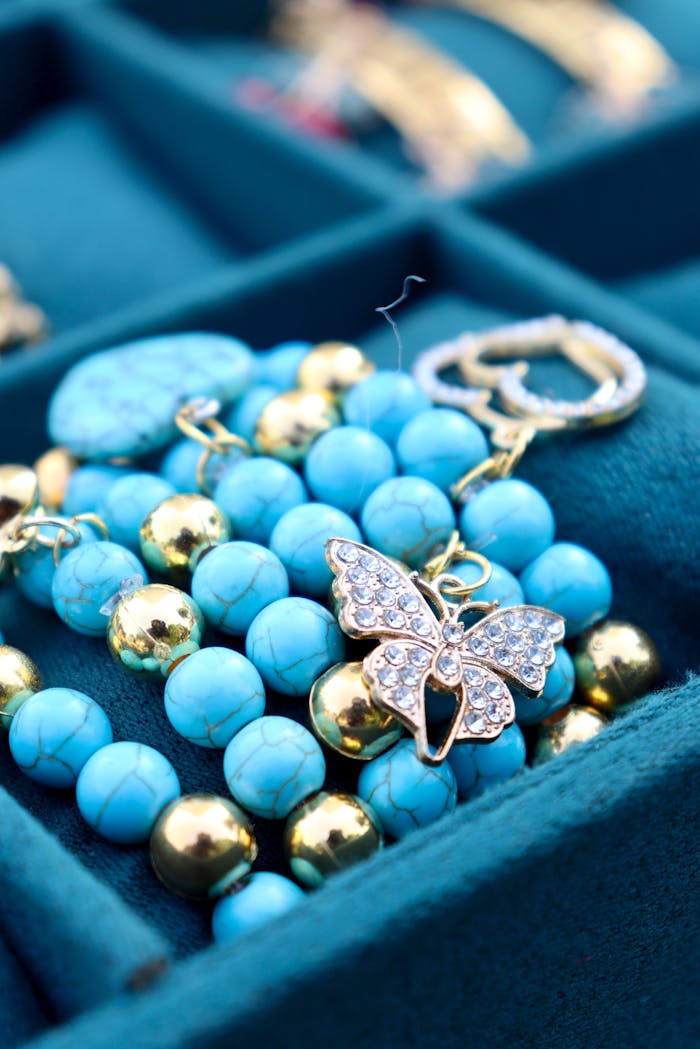 Close-up of turquoise and gold bead bracelet with a crystal butterfly charm in a jewelry box.