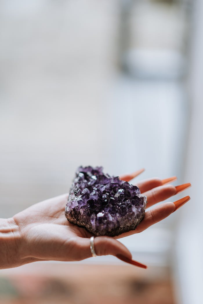 Hand of anonymous female with colorful uncut stone with purple crystals while standing in light spacious room on blurred background
